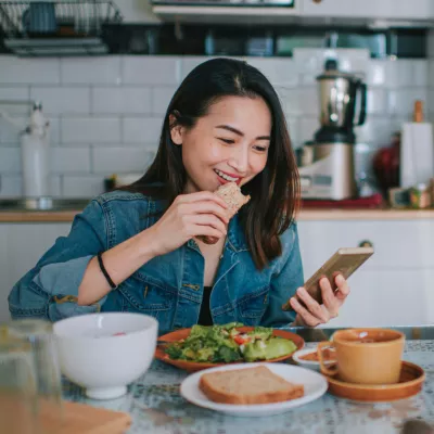 A Woman Smile at Her Mobile Device as She Eats a Balanced Breakfast