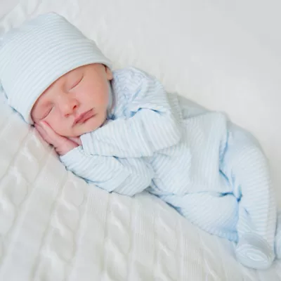 Newborn in blue clothes and a blue hat on a white blanket