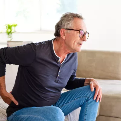 Older man holding his back with his hand while getting up off the couch.