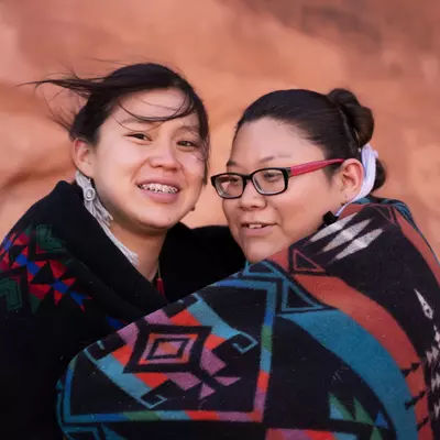 Native American mother and daughter wrapped in a blanket together while outdoors.