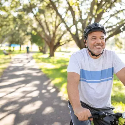 Smiling man riding his bike through the park.