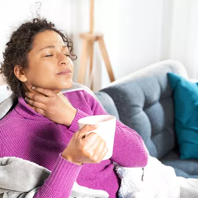 woman rubs sore throat and drinks tea