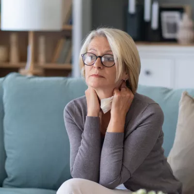 Woman sitting on a couch at home while holding a tissue.