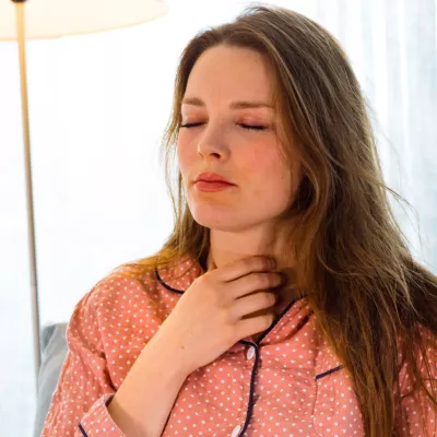 Woman touching her sour throat while sitting at home while wearing pajamas.