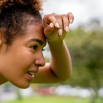 A woman wipes her brow while taking a break from exercising outdoors.