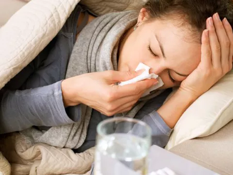 A woman laying in bed with the flu, water and medicine on her nightstand.