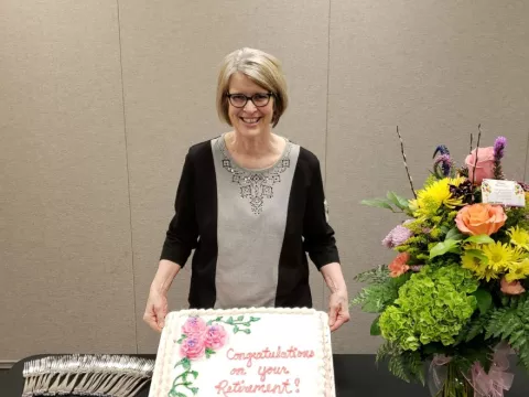 A woman standing behind a cake that has her name.