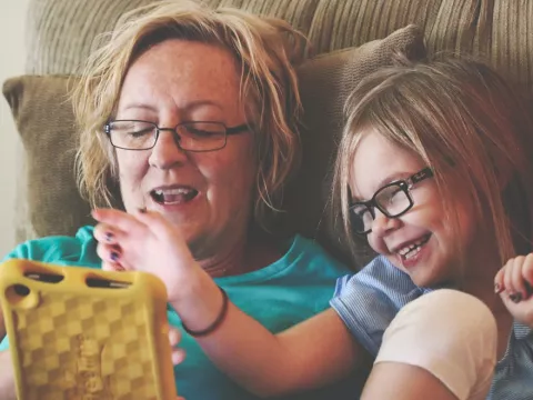 A grandmother playing with her grand-daughter in the couch with a tablet. 