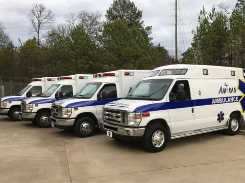 Four medical transport vans with the words Amtran sit in a parking lot