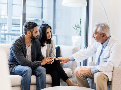 A couple, sitting with a doctor who is comforting them.