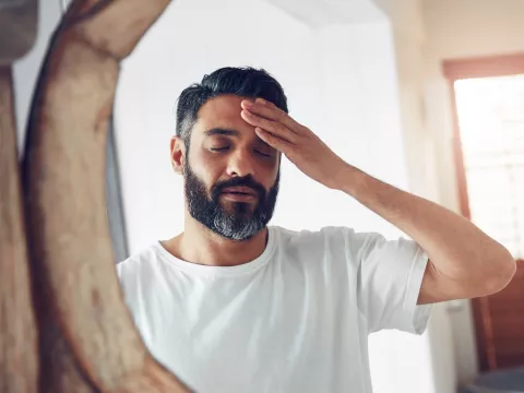 A man is standing in front of a mirror, rubbing his head, stressed out.