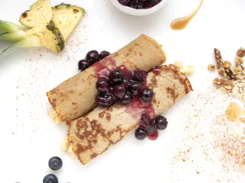 Two crepes covered with blueberry sauce next to pineapple garnish