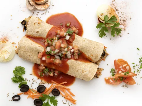 Two enchiladas with sauce and parsley, carrot, and olive garnishes