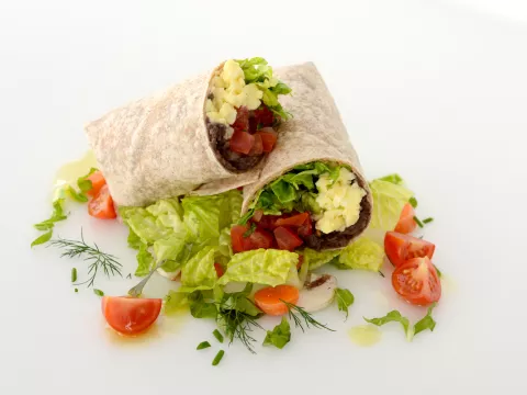 Breakfast burrito halved and stacked with tomato and green garnishes