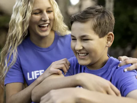 A boy and his mother smiling together while outside.