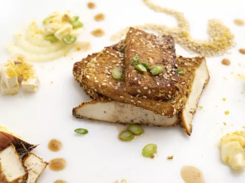 three tofu steaks on white surface with nutritional yeast garnish