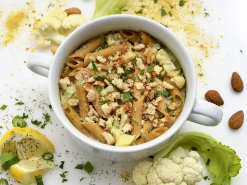 White bowl filled with cauliflower-pasta next to garnishes