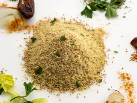 Mound of chicken-style seasoning on white surface surrounded by garnishes