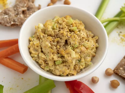 White bowl of chickpea chicken-style salad with vegetable stick garnishes