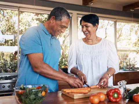 A couple cutting up carrots for a salad while in a kitchen.