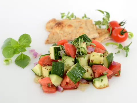 Mound of cucumber salad with pita and tomato garnishes