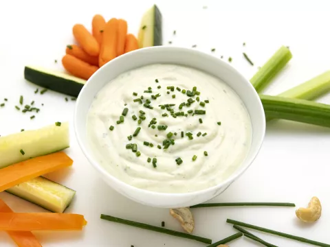 Bowl of sour cream surrounded by vegetable sticks.