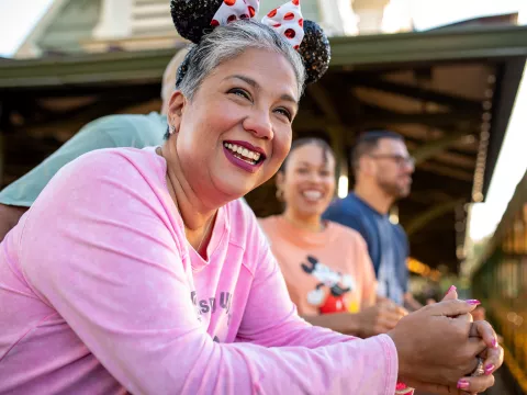 A senior woman smiling and wearing a Minnie Mouse headband in the foreground with her family in the background at Walt Disney World® Resort.