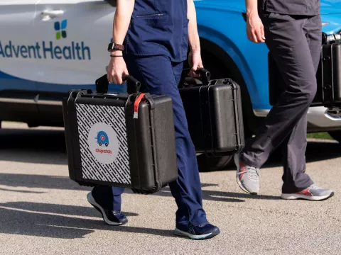 2 people in scrubs carry medical equipment in DispatchHealth cases