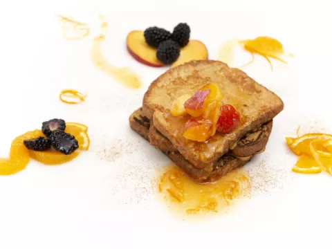 three stacked slices of french toast, topped with a fruit sauce 