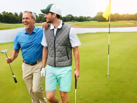 Two grown men walking away from a golf hole