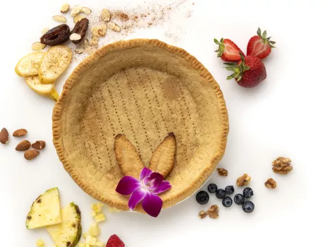 Whole, empty pie crust decorated with fruit chunks and an orchid.