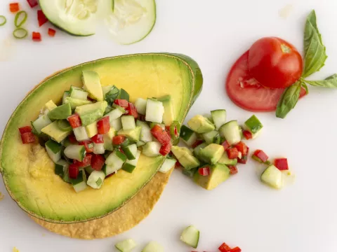 Half an avocado filled with avocado salsa on a white surface