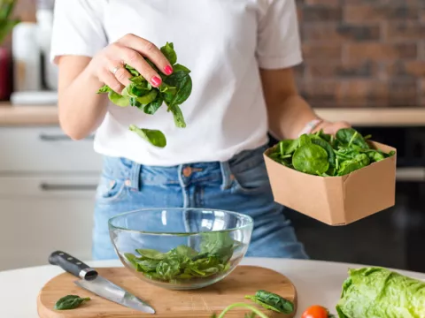 woman puts spinach in a clear glass bowl