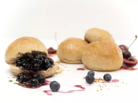 four fresh baked rolls, one covered in blueberries with a fruit syrup