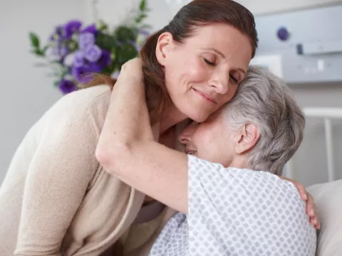 An adult daughter hugs her mom in the hospital.