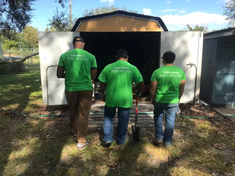 Three volunteers in front of a shed