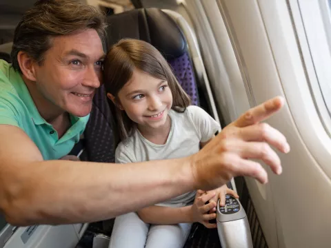 A father and daughter looking out the window of an airplane.