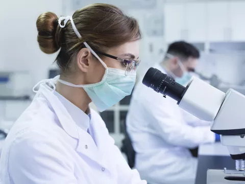 A woman looking through a microscope in a lab.