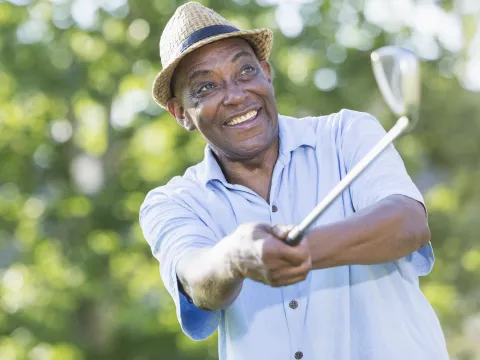 An older man swings a club on the golf course.