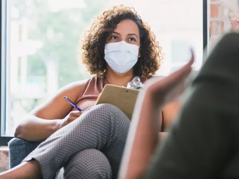 A mental health provider visits with a patient wearing a mask. 