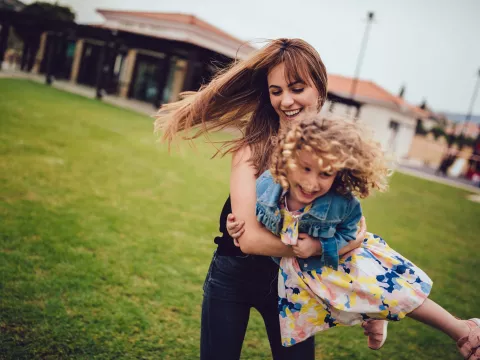 Mom spins her young daughter around in the grass