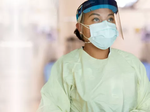 A nurse, dressed in proper personal protection equipment, stands praying.