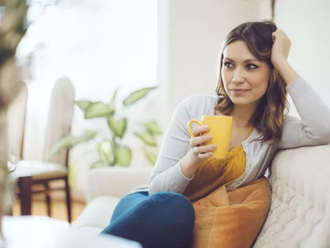 A young woman sits on her couch at home drinking her coffee