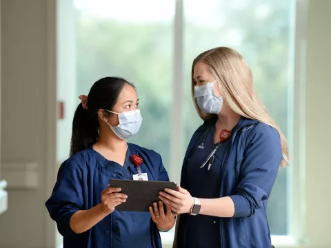 Two nurses looking at each other, holding a tablet