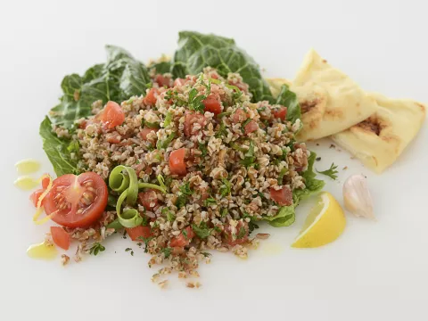 Mound of tabbouleh salad with pita, lettuce, tomato, and lemon garnishes