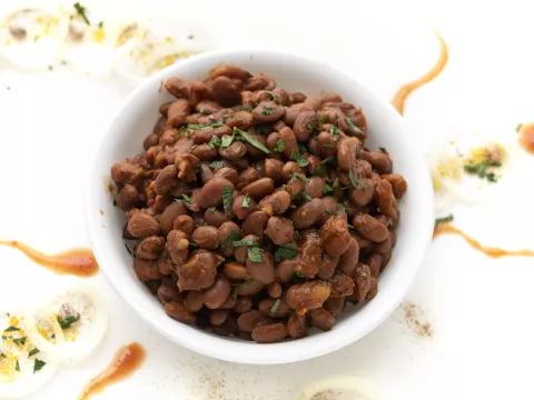 White bowl of baked beans on white, garnished counter