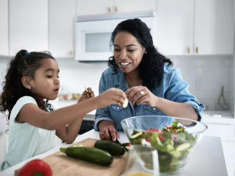 A mother and daughter prepare a salad at home. 