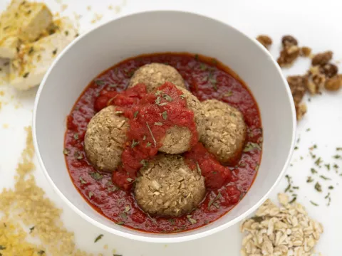 Bowl of nut balls in red sauce with breadcrumb decoration