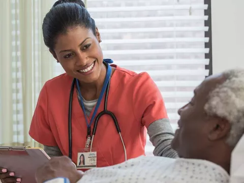 Nurse holding clipboard and standing by elderly patient's bedside