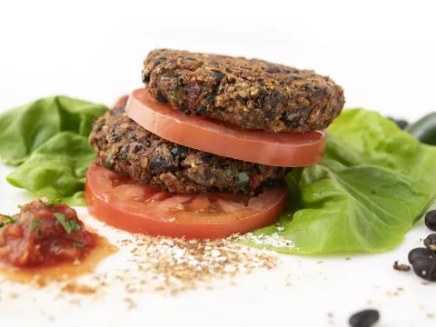 Two stacked bean burgers patties, sliced tomatoes, and lettuce leaves